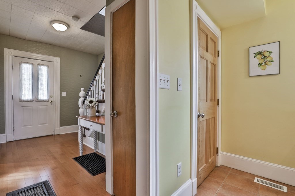 Entry hall with hardwood floors, a white front door, staircase, and adjoining tiled room.