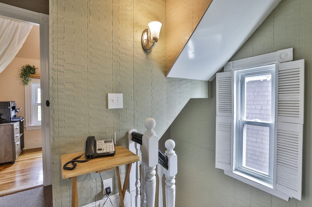 Upstairs landing with a shuttered window, sloped ceiling, and telephone table beside the stair railing.