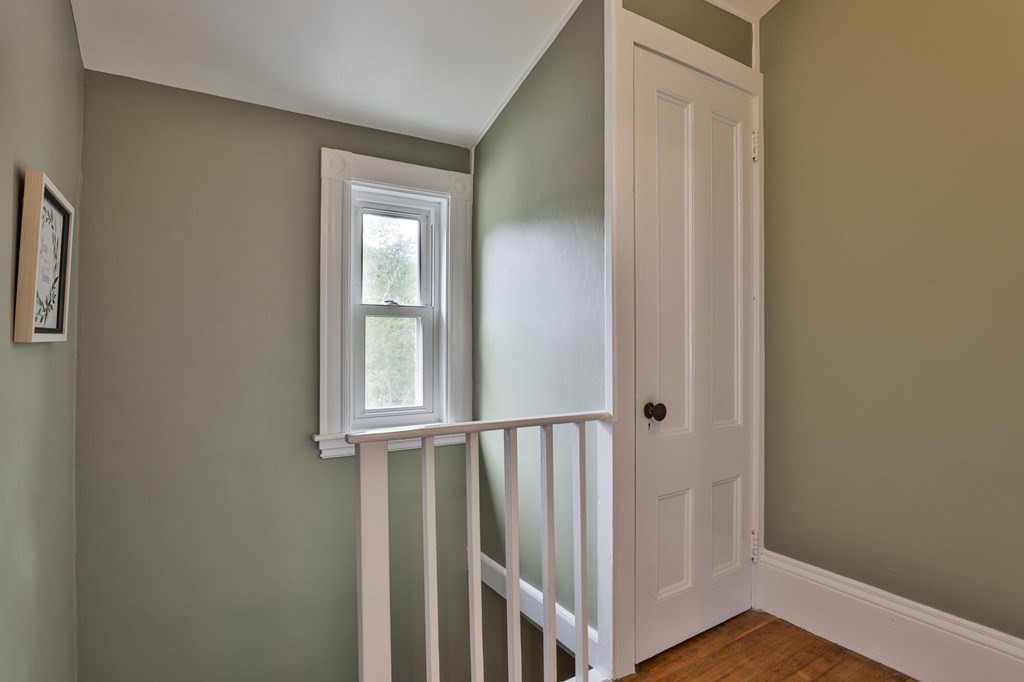 Upstairs landing with a white stair railing, sage-green walls, and a tall window.