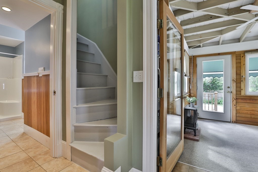 Staircase between a tiled bathroom and wood-paneled sunroom with a freestanding stove.