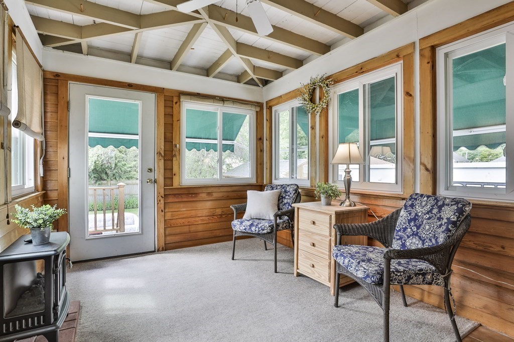 Wood-paneled sunroom with exposed beams, wicker chairs, and windows overlooking the yard.