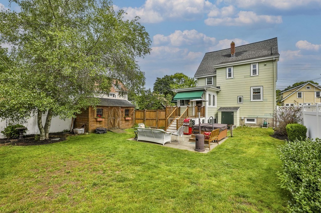 Two-story pale green house behind a lawn, with a patio, hot tub, and wooden shed.