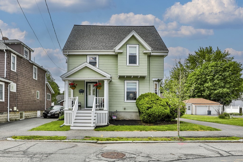 Pale green two-story house with a covered porch, white steps, and shrubs along the front lawn.