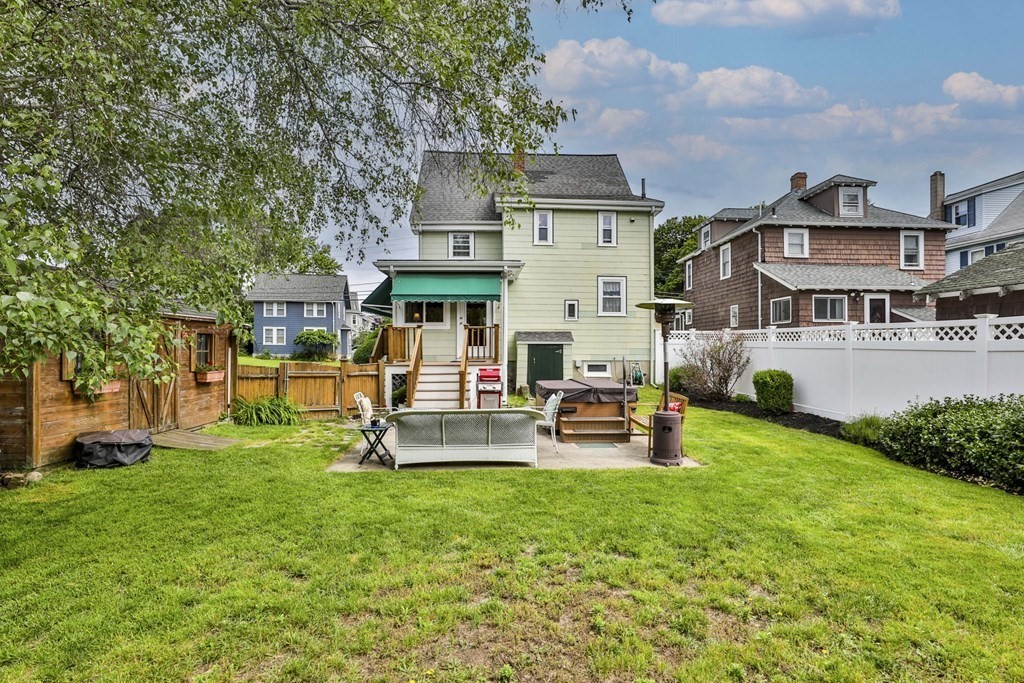 Backyard of a pale green house with a furnished patio, broad lawn, and fenced yard.