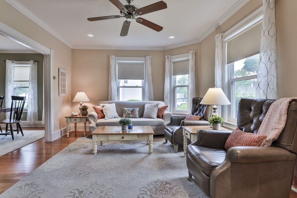 Furnished living room with a gray sofa, leather armchairs, and large curtained windows.