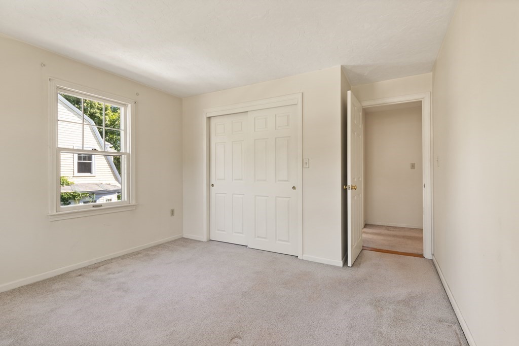 Empty bedroom with a white sliding-door closet, light carpet, and a window.