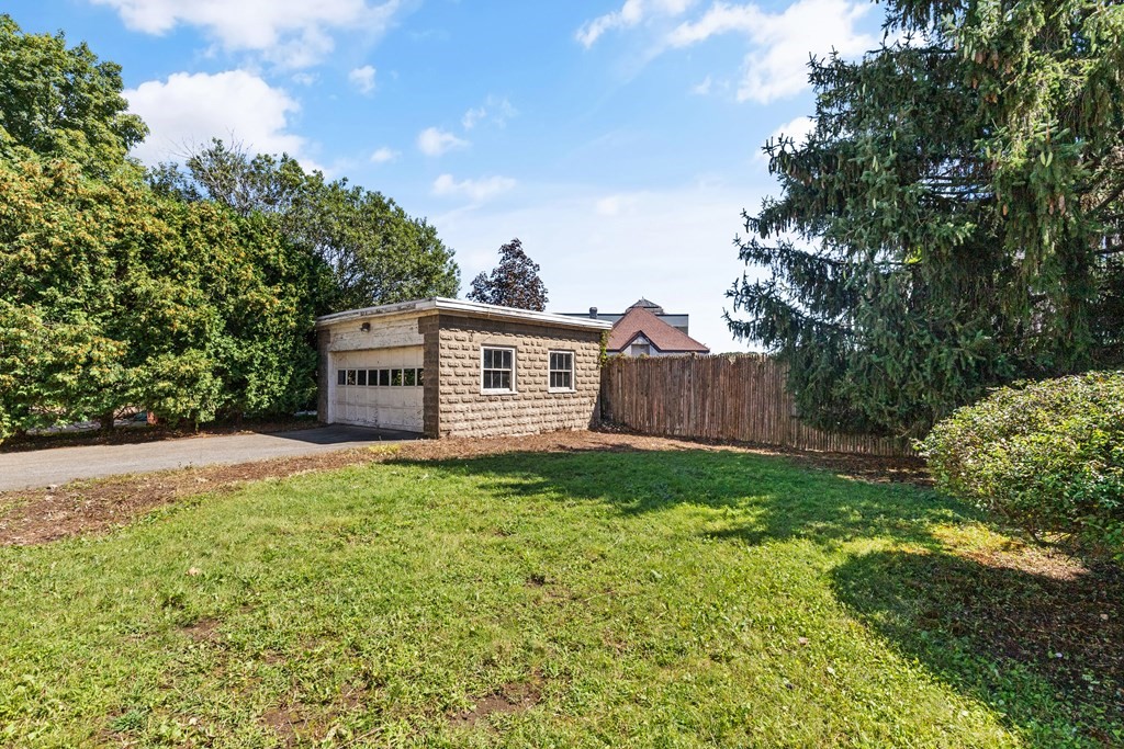 Detached stone garage beside a green lawn and wooden fence.