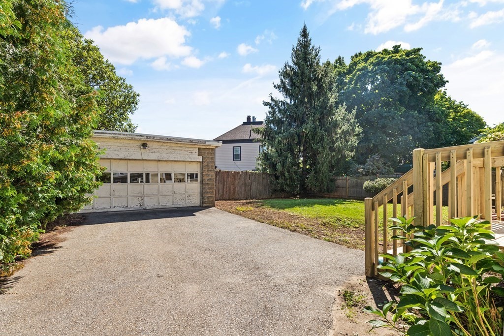 Driveway leading to a detached garage beside a wooden deck railing and leafy yard.