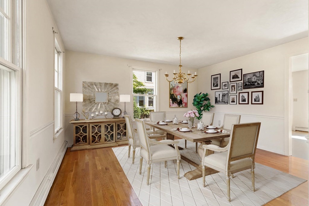 Dining room with a set table, chandelier, tall windows, and framed artwork.