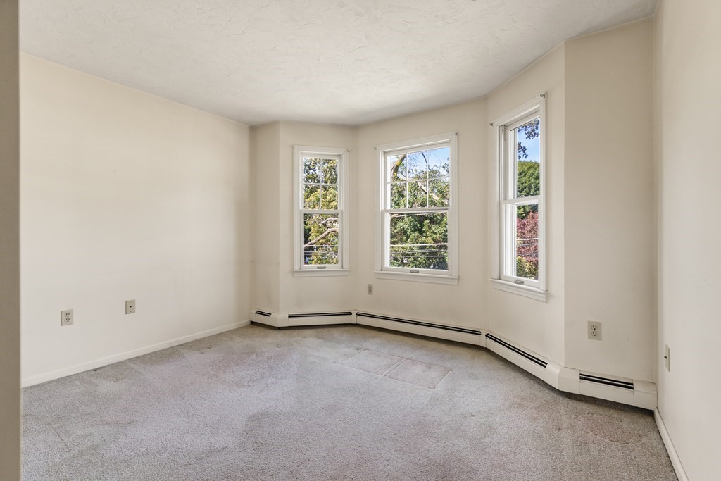 Empty carpeted room with three windows and baseboard heating.