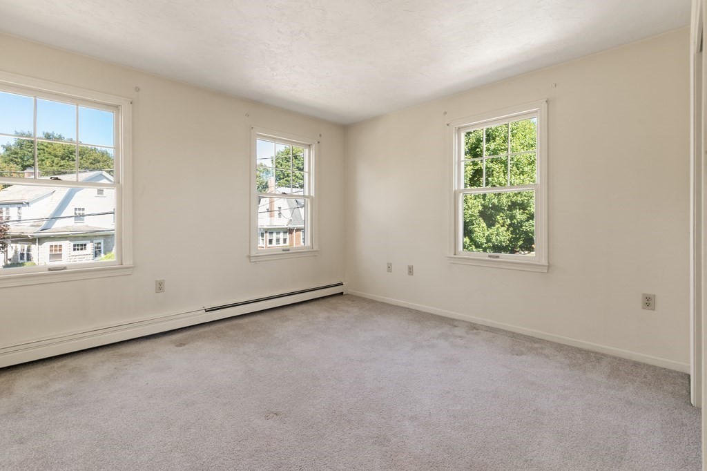 Empty carpeted room with three windows and baseboard heating.