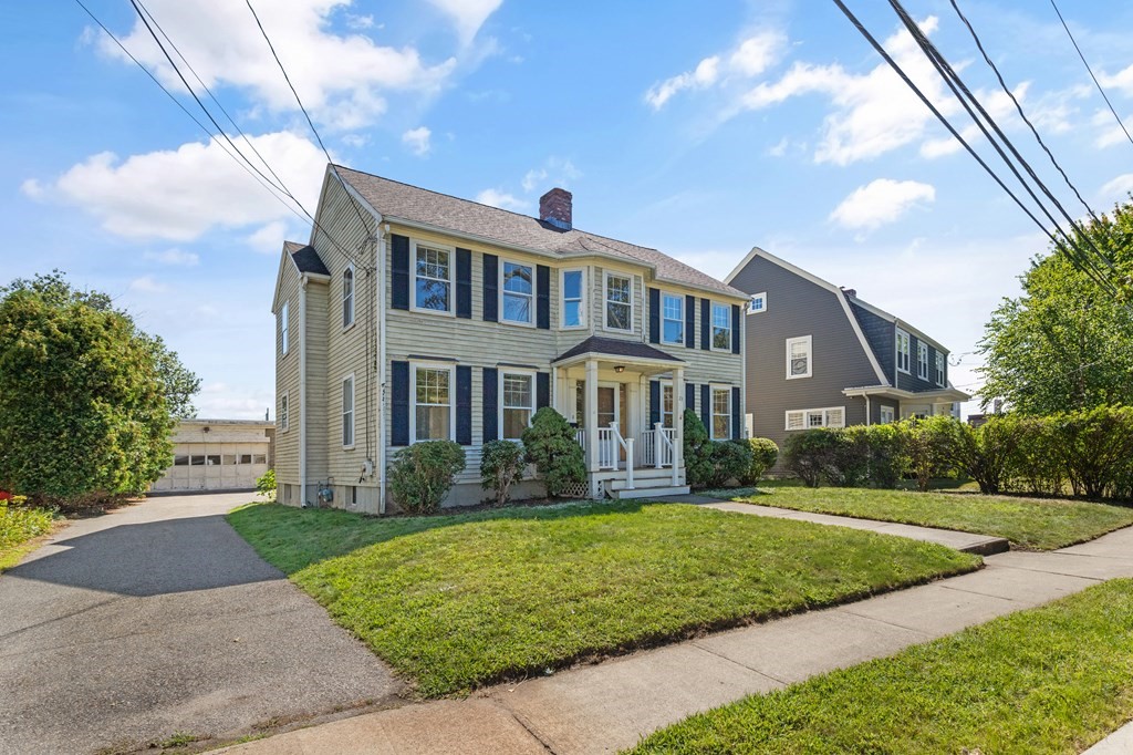 Two-story light-colored house with dark shutters, a covered porch, and a driveway.