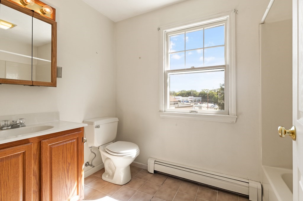 Bathroom with a wood vanity, toilet, tiled floor, and large street-facing window.