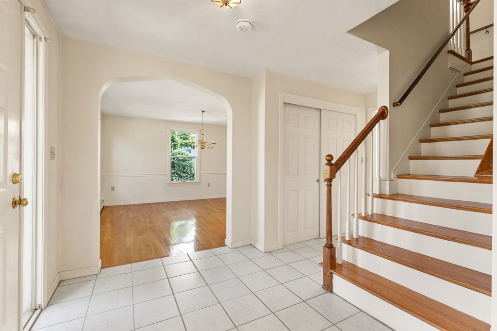 Vacant entryway with a wood-and-white staircase and arched opening to a hardwood dining room.
