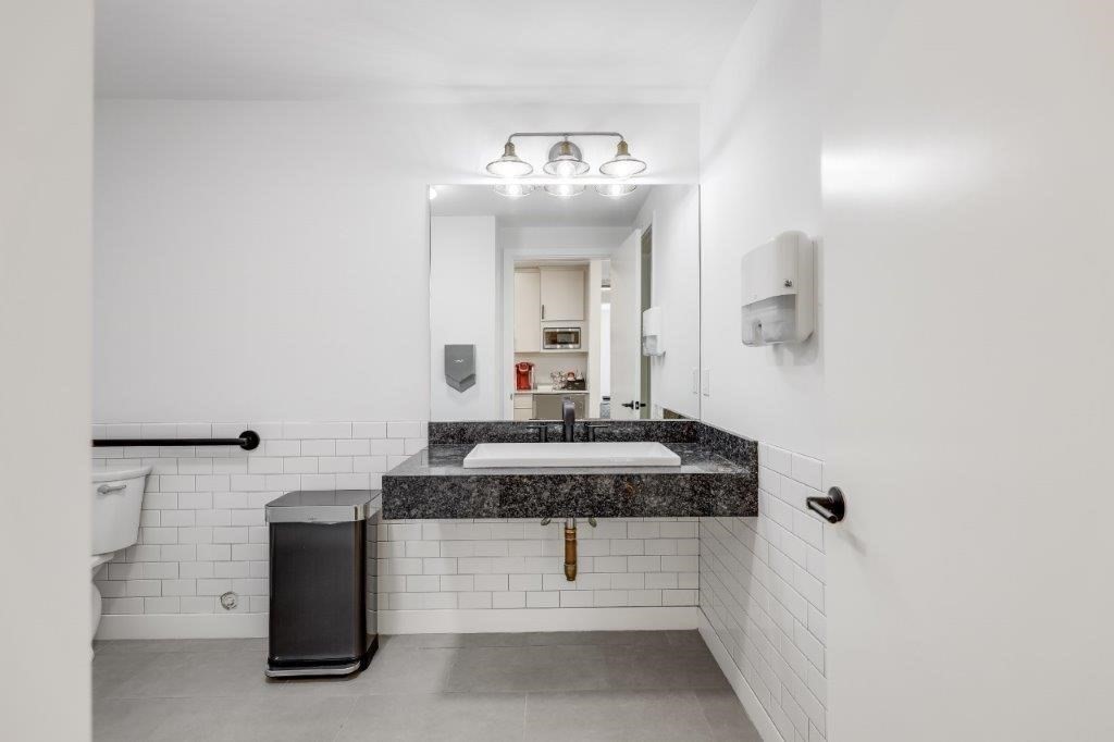 Bathroom with a vessel sink, dark granite counter, large mirror, and white subway tile.