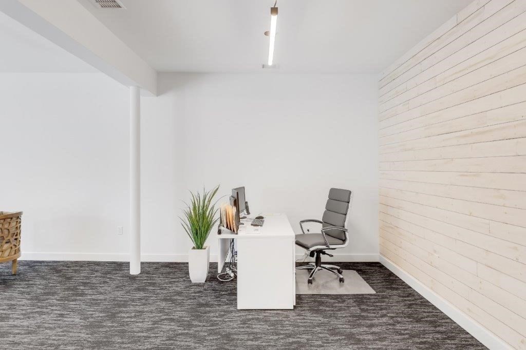 Furnished office with a white desk, gray rolling chair, and pale wood-plank accent wall.