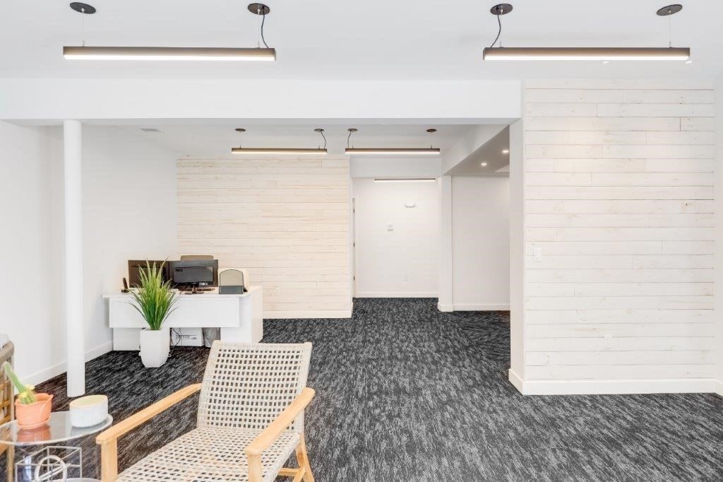 Furnished reception area with a white desk, woven lounge chair, and dark patterned carpet.