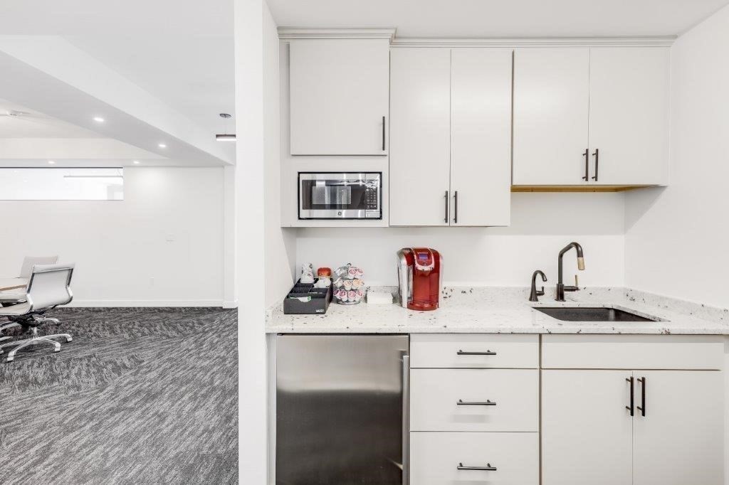 Modern kitchenette with white cabinetry, stainless-steel dishwasher, and speckled countertop beside an office area.