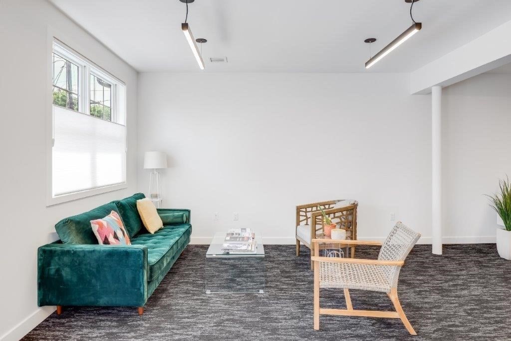 Furnished lounge with a teal velvet sofa, glass coffee table, and woven chairs.