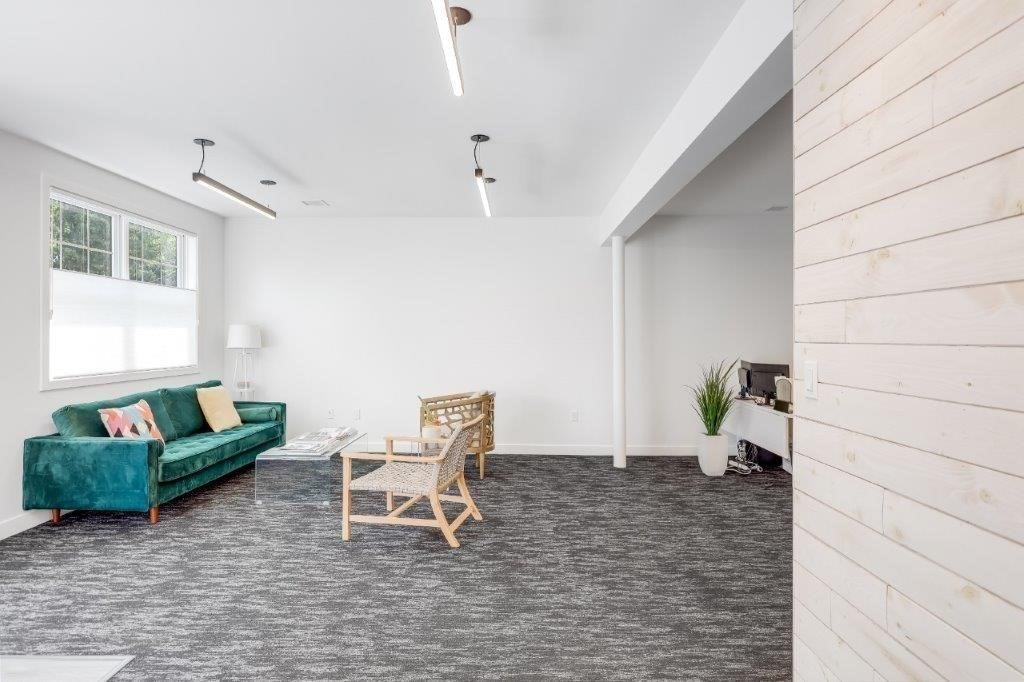 Furnished lounge with a teal sofa, wicker chairs, and dark patterned carpet.
