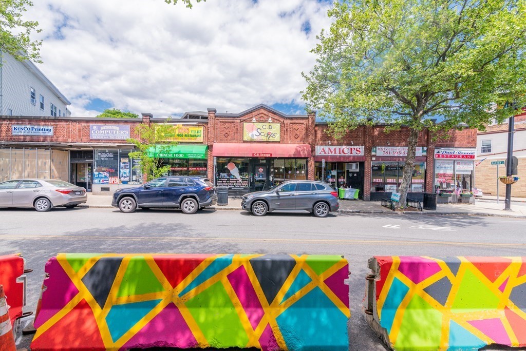 Row of brick storefronts behind colorful painted traffic barriers.
