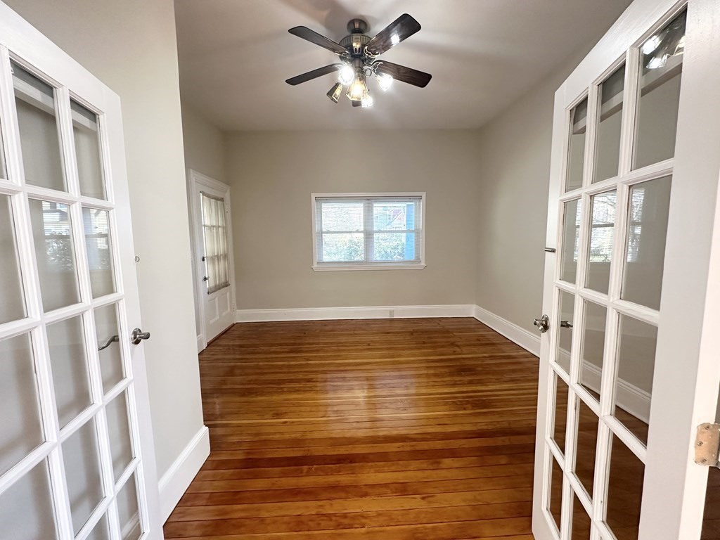 Empty room with polished hardwood floors, a ceiling fan, and windows on three sides.