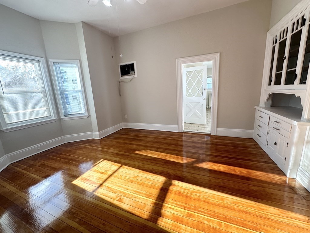 Unfurnished room with polished hardwood floors, two windows, and a built-in white cabinet.
