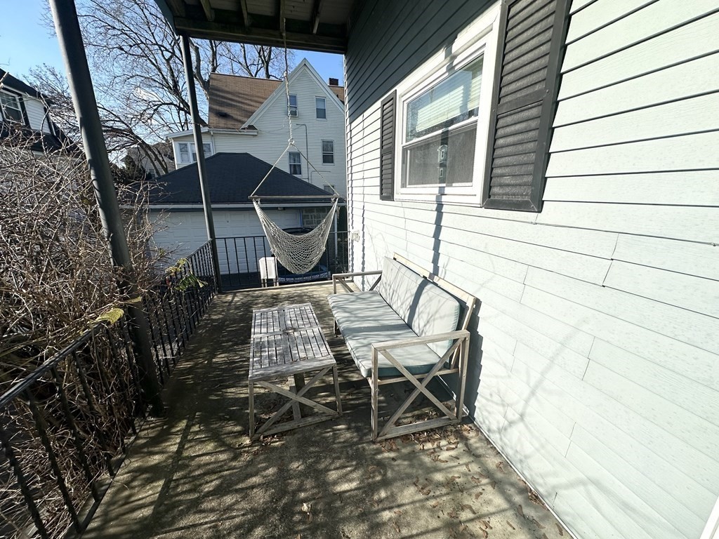 Outdoor deck with a wooden bench, table, black railing, and hanging hammock beside a light-sided house.