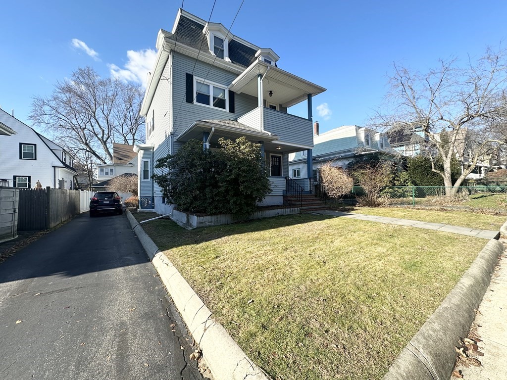 Gray multi-story house with a covered porch, front lawn, and driveway.