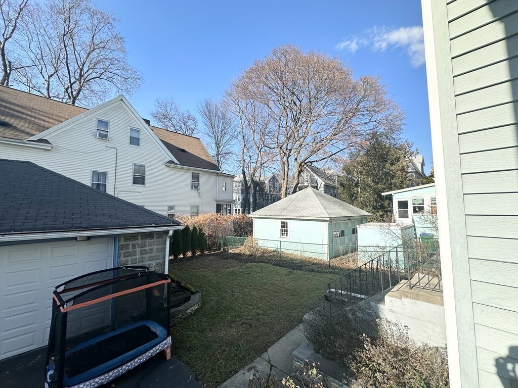 Backyard with a grassy lawn, detached garage, and small outbuilding beneath leafless trees.