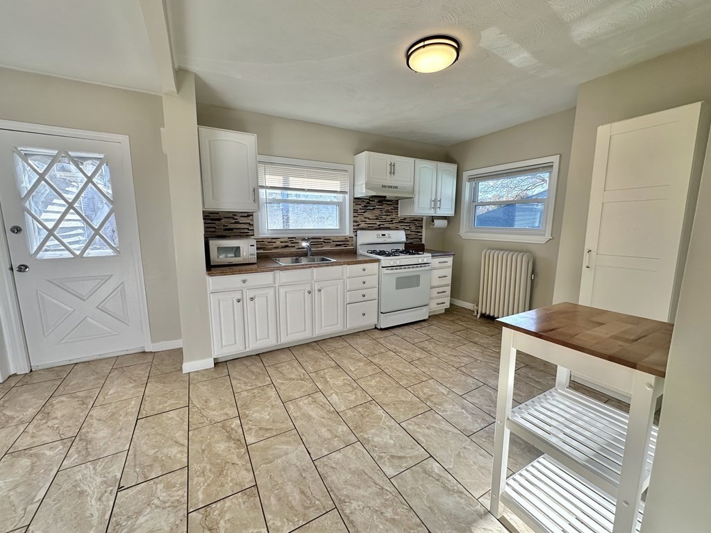 Kitchen with white cabinets, mosaic tile backsplash, patterned floor, and butcher-block utility cart.