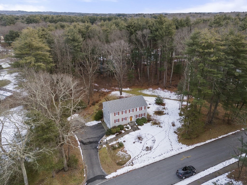 Gray two-story colonial with red shutters, a driveway, and patchy snow on a wooded lot.