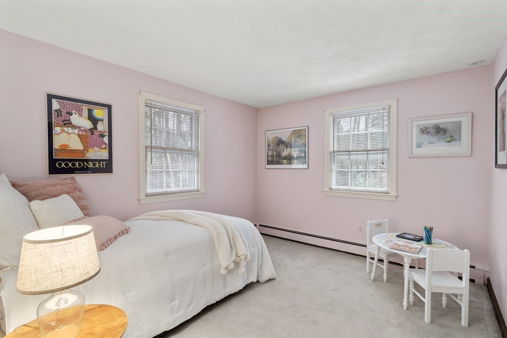 Pink bedroom with a white bed, two curtained windows, and a small children's table and chairs.