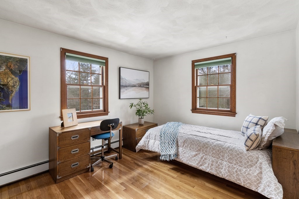 Bedroom with a single bed, two wood-trimmed windows, and a desk on hardwood floors.