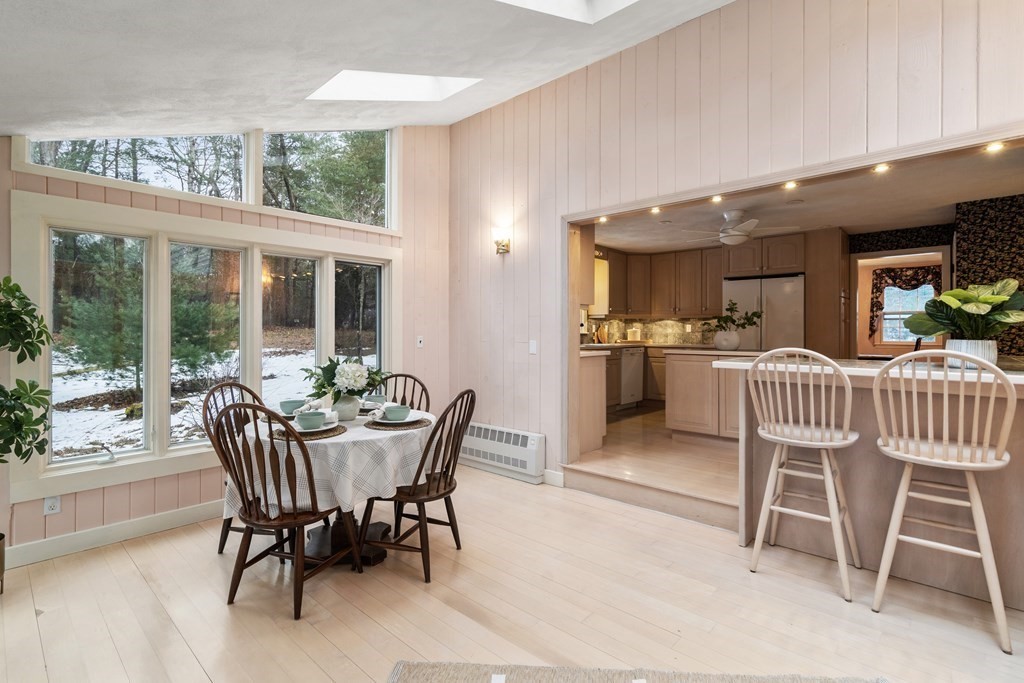 Dining area with a round table beside tall windows, opening to a kitchen with a breakfast bar.