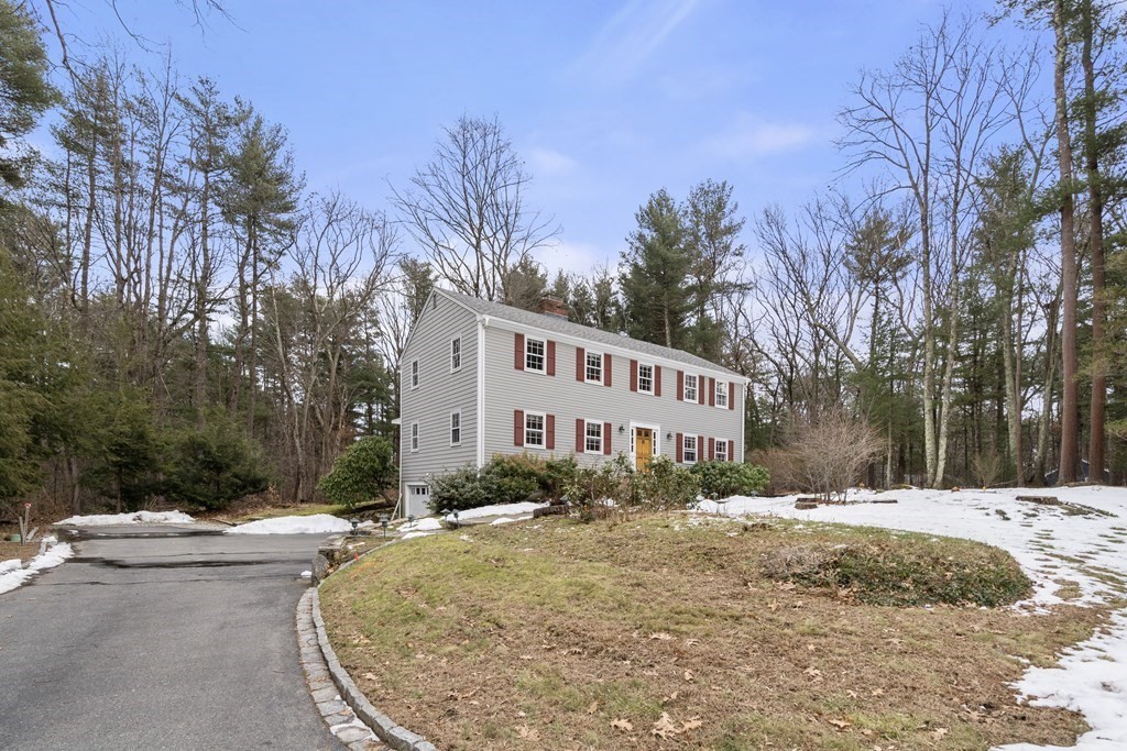 Gray two-story home with red shutters and a yellow front door, surrounded by trees.