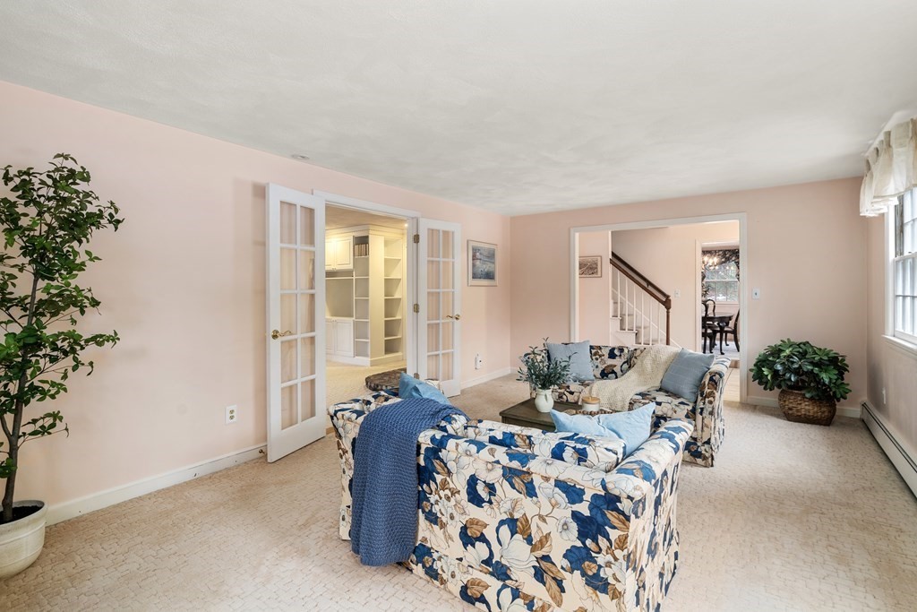 Living room with floral sofas, pale pink walls, and French doors opening to a bright adjoining room.