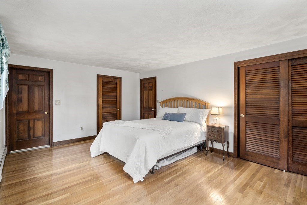 Bedroom with a white bed, hardwood floors, and dark wood doors and closet.
