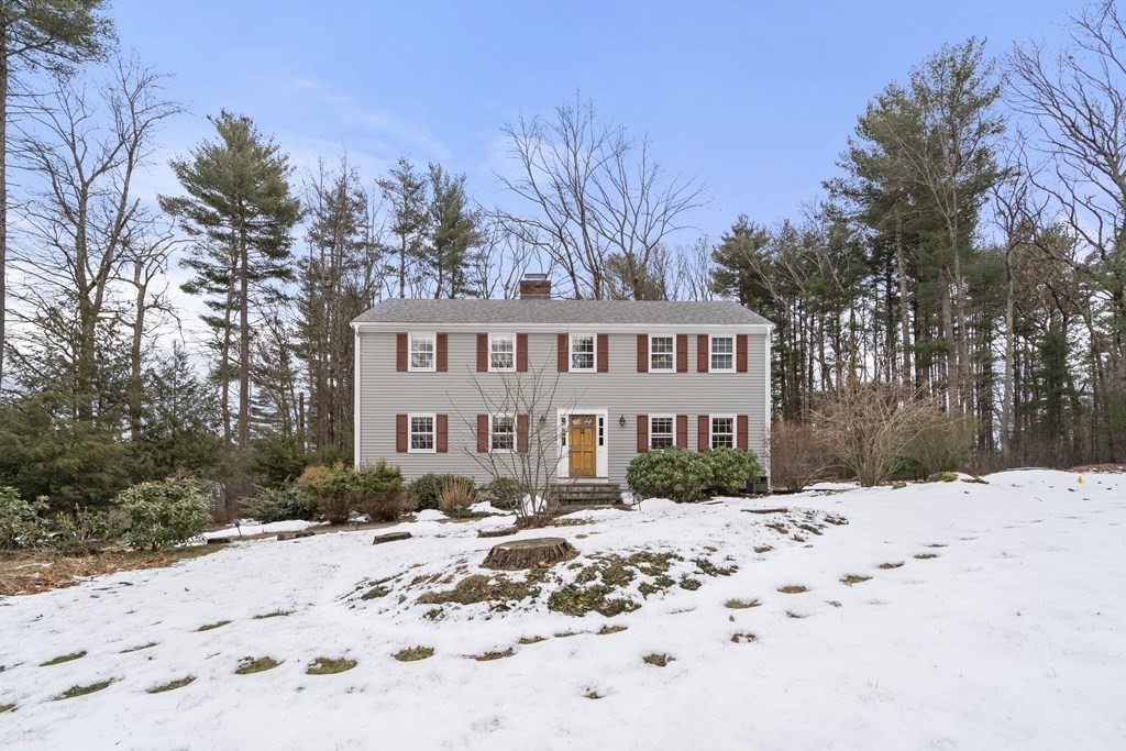Gray two-story house with red shutters and a wooden front door, set behind a snow-covered lawn.