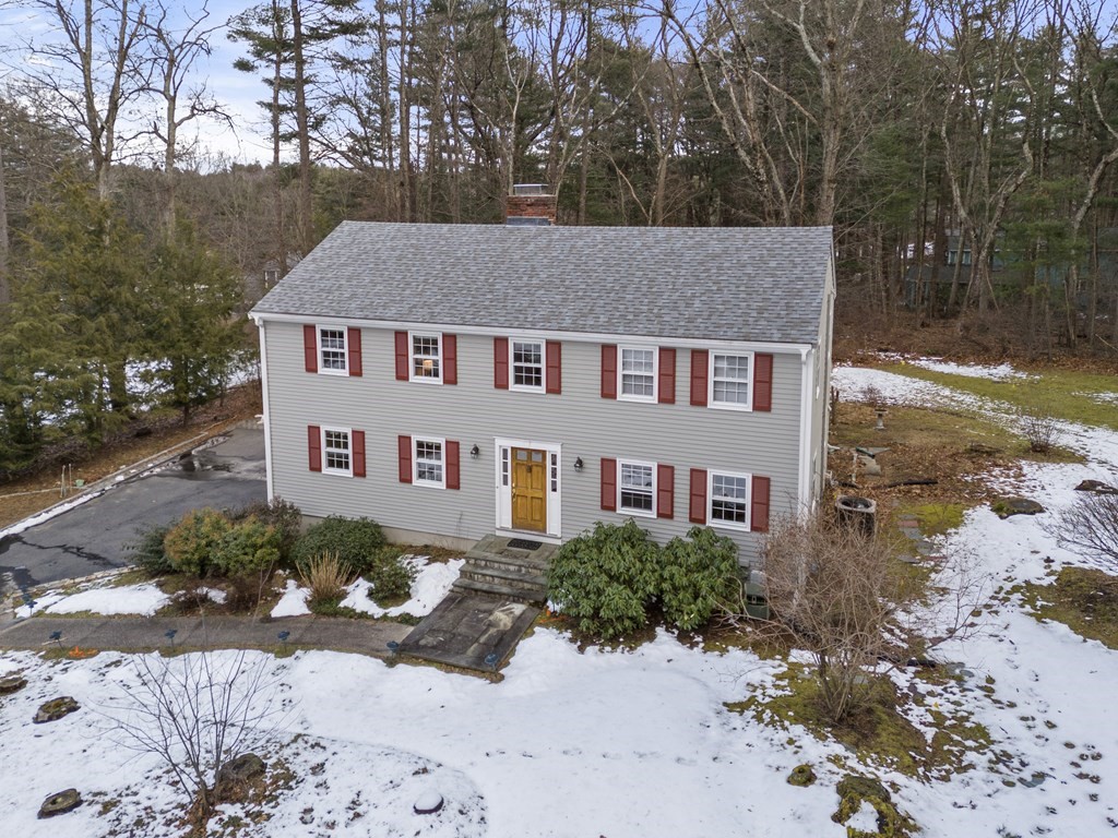 Two-story gray house with red shutters and yellow door, viewed from above amid a patchy snowy yard.