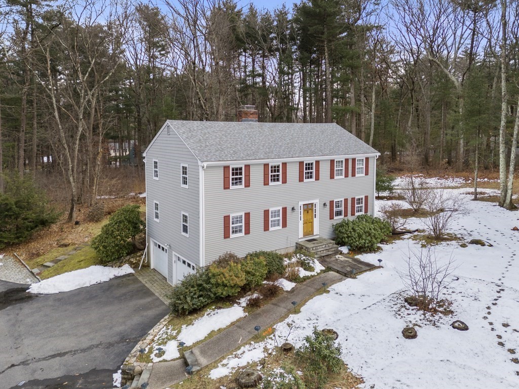 Two-story gray house with red shutters, yellow front door, and attached garage amid patchy snow.