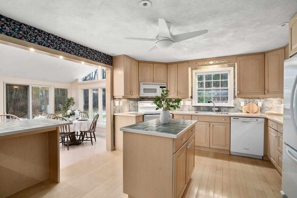 Kitchen with a tiled island and light wood cabinets opening to a window-lined dining area.