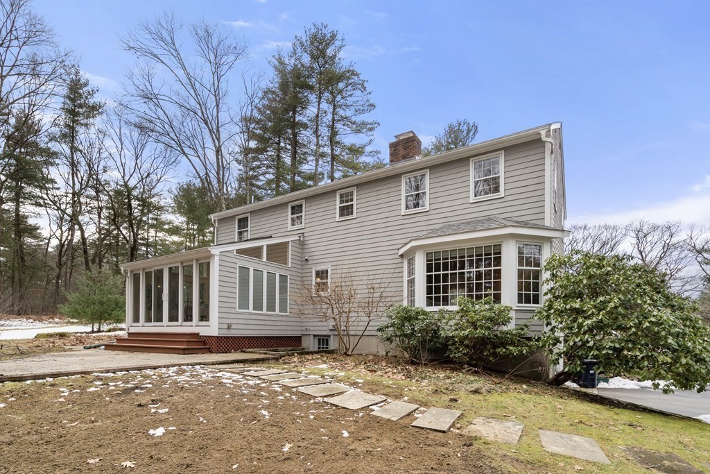 Two-story gray house with a glass sunroom and large bay window, surrounded by bare trees.