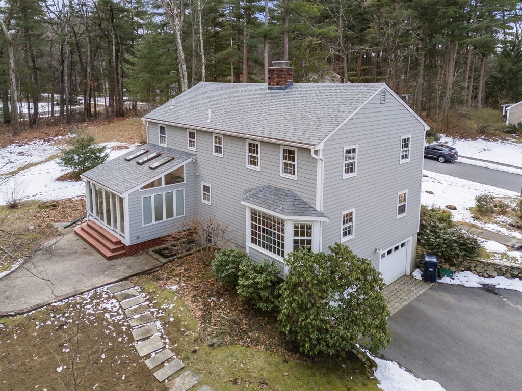 Gray two-story house with a glass-enclosed sunroom, brick chimney, and snow patches in the yard.
