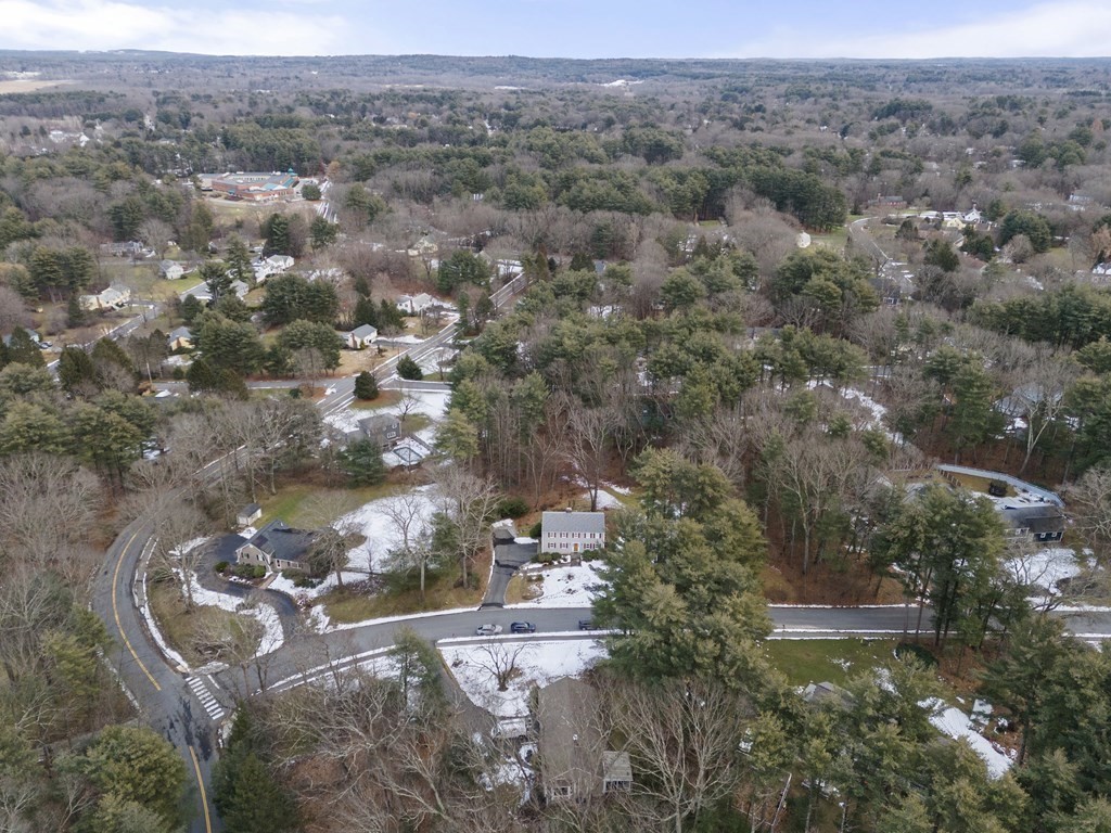 Aerial view of a white two-story home amid wooded, snow-dusted suburban lots.