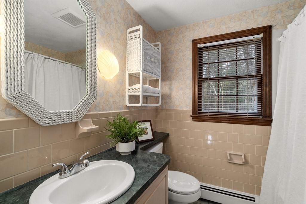 Bathroom with peach tile, a woven-frame mirror, and a dark countertop beneath a window with wood blinds.