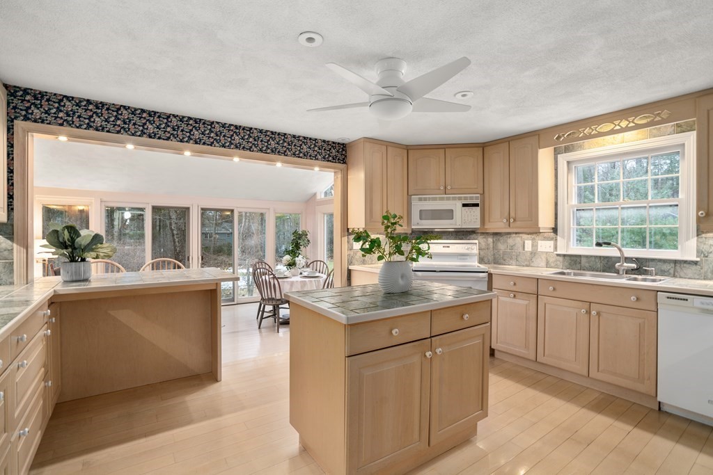 Kitchen with light wood cabinetry, a central island, and a dining area beside large windows.