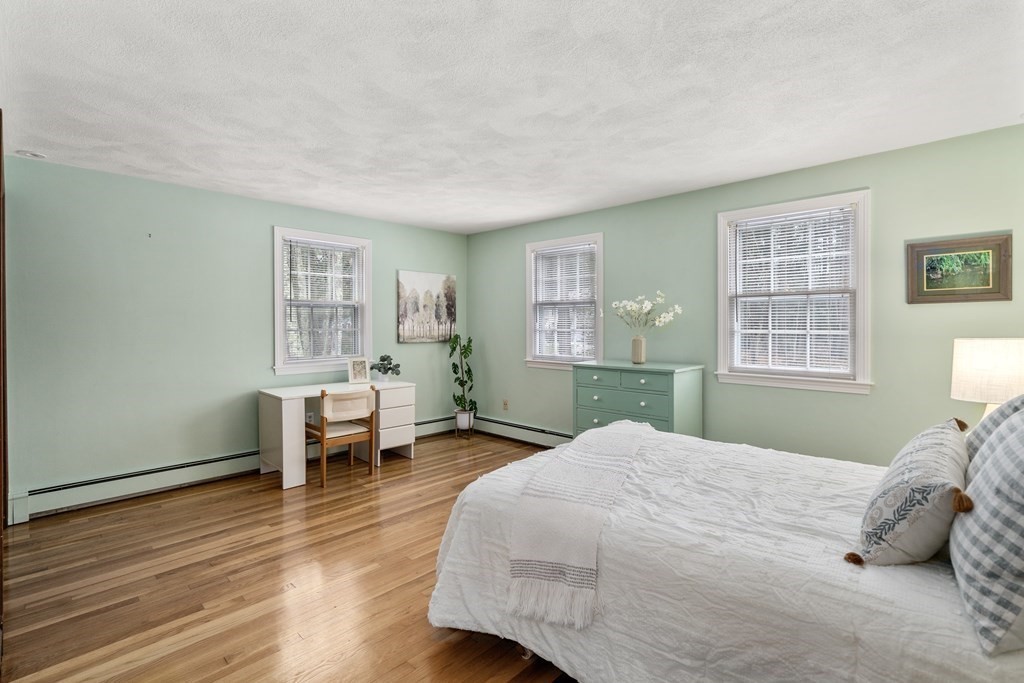 Bedroom with pale green walls, hardwood floors, three windows, and a white bed.
