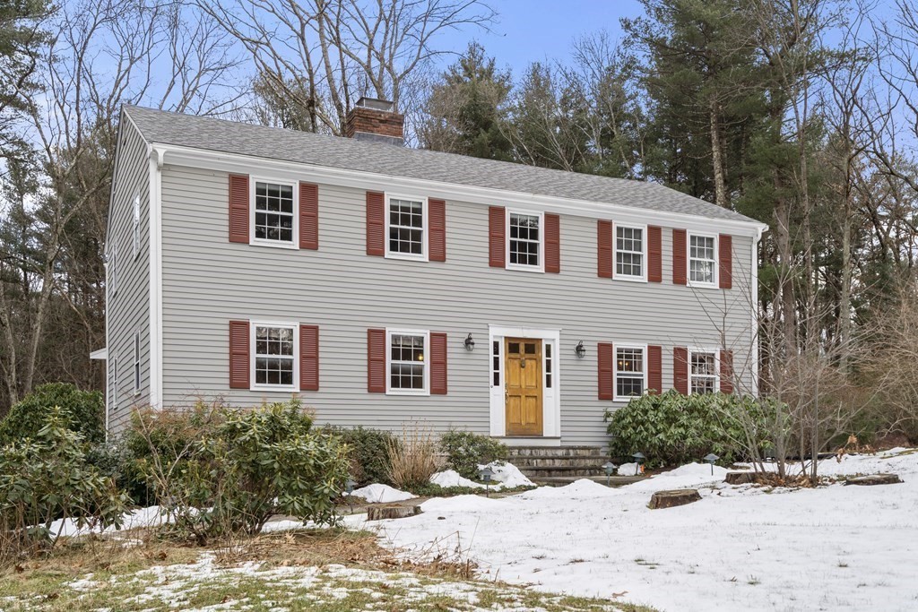 Two-story gray house with red shutters and a wooden front door in a snow-dusted yard.