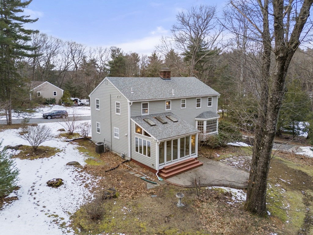 Gray two-story house with a glass sunroom and red steps, surrounded by leafless trees and patchy snow.